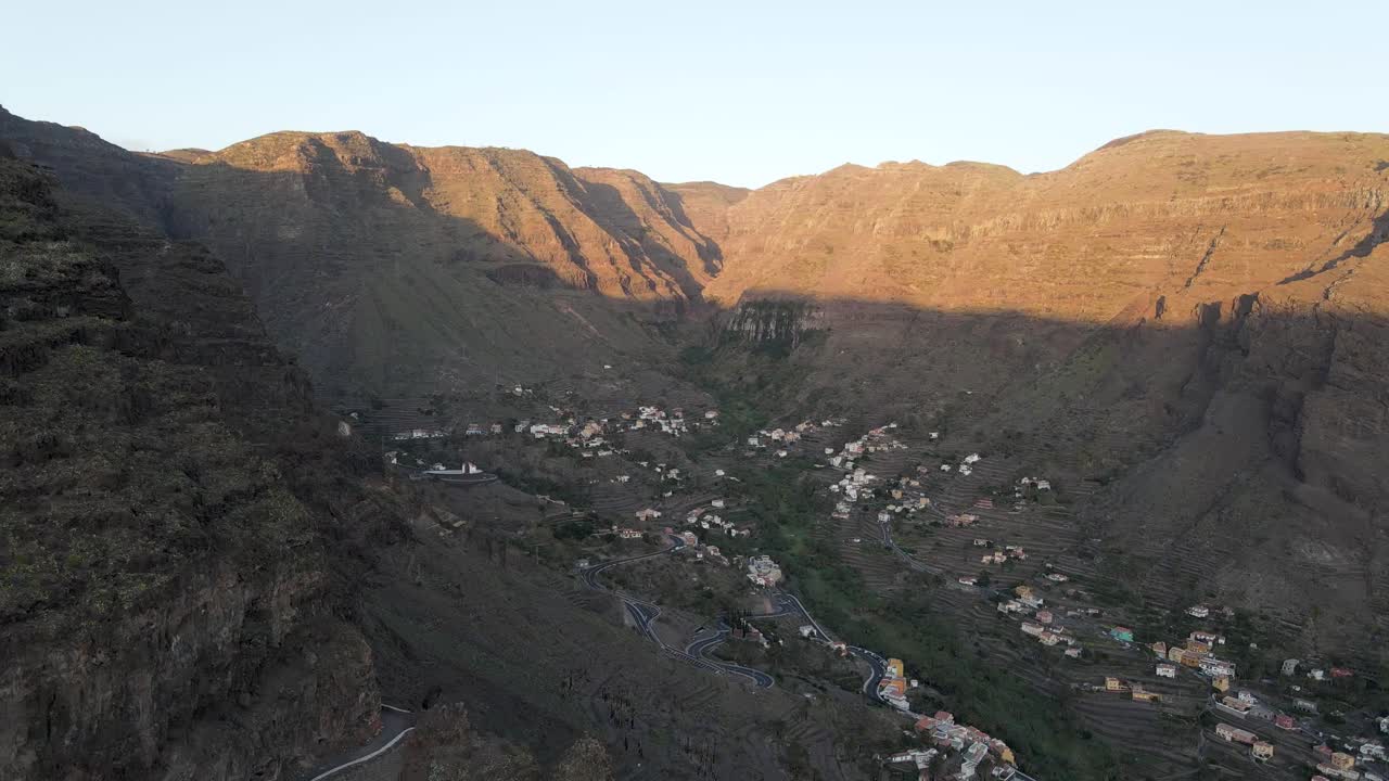 Gran Rey vadisi, La Gomera, Kanarya Adaları'nda, gün doğumu sırasında dik, engebeli dağların ortasındaki bir köyün havadan drone çekimi