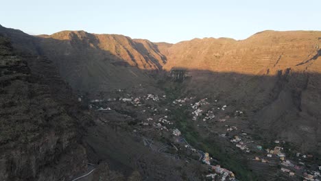 aerial drone footage of village in the middle of steep rugged mountains during sunrise in gran rey valley, la gomera, canary islands