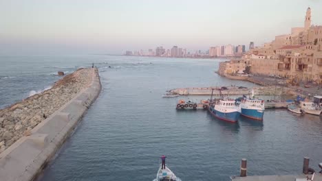 jaffa harbor with boats moving showing masonry architecture and medieval influence while in the far distance is the modern skyline of tel aviv circa march 2019