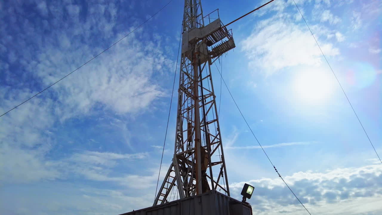 Oil production derrick in the field. Low angle view at the tower at backdrop of blue sky with light clouds.