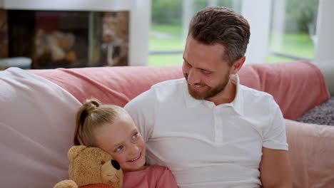 Father-looking-at-adorable-daughter-on-sofa.-Happy-man-talking-with-little-girl