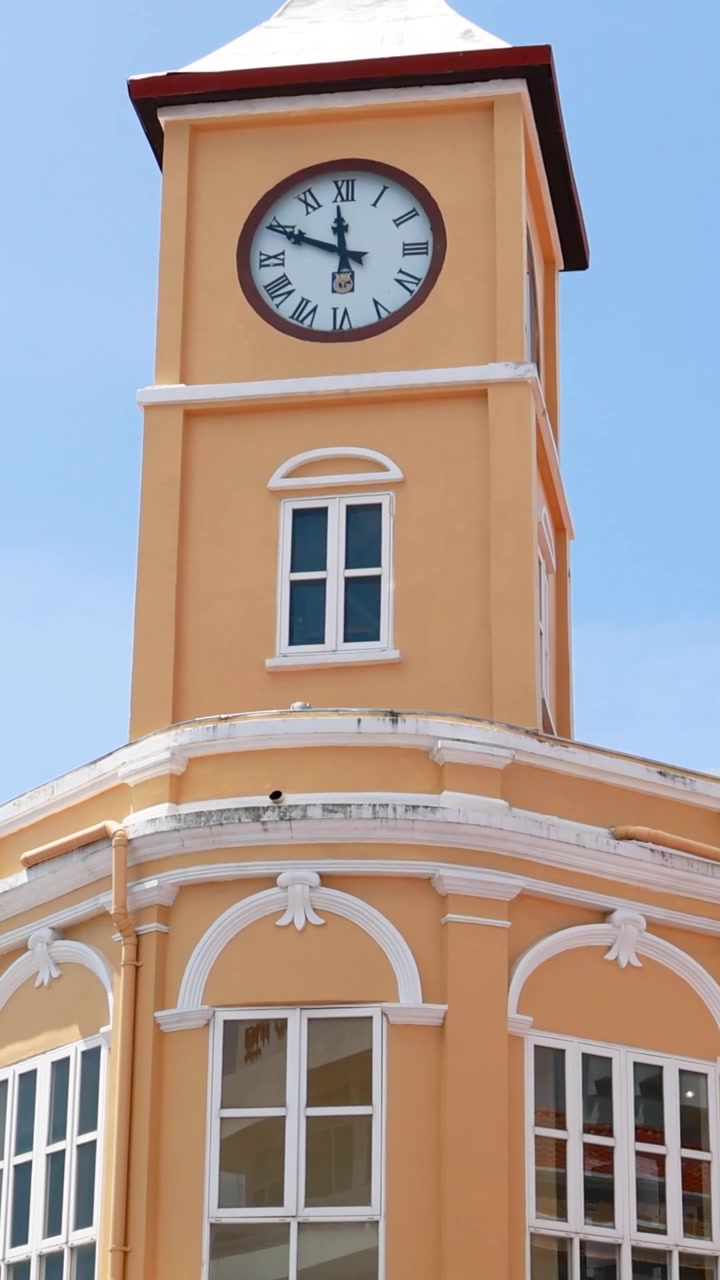 A tall colonial-style clock tower stands against a blue sky as vehicles pass below.