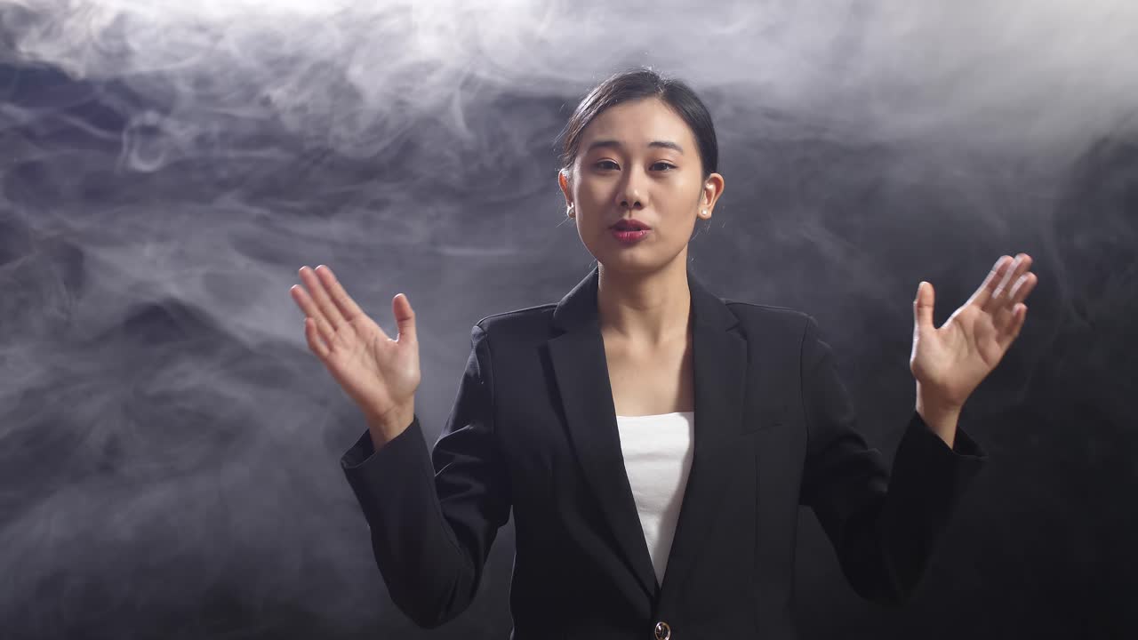블랙 스크린 스튜디오 에서 연설 하는 동안 손 을 고 있는 비즈니스 슈트 를 입은 아시아 여성