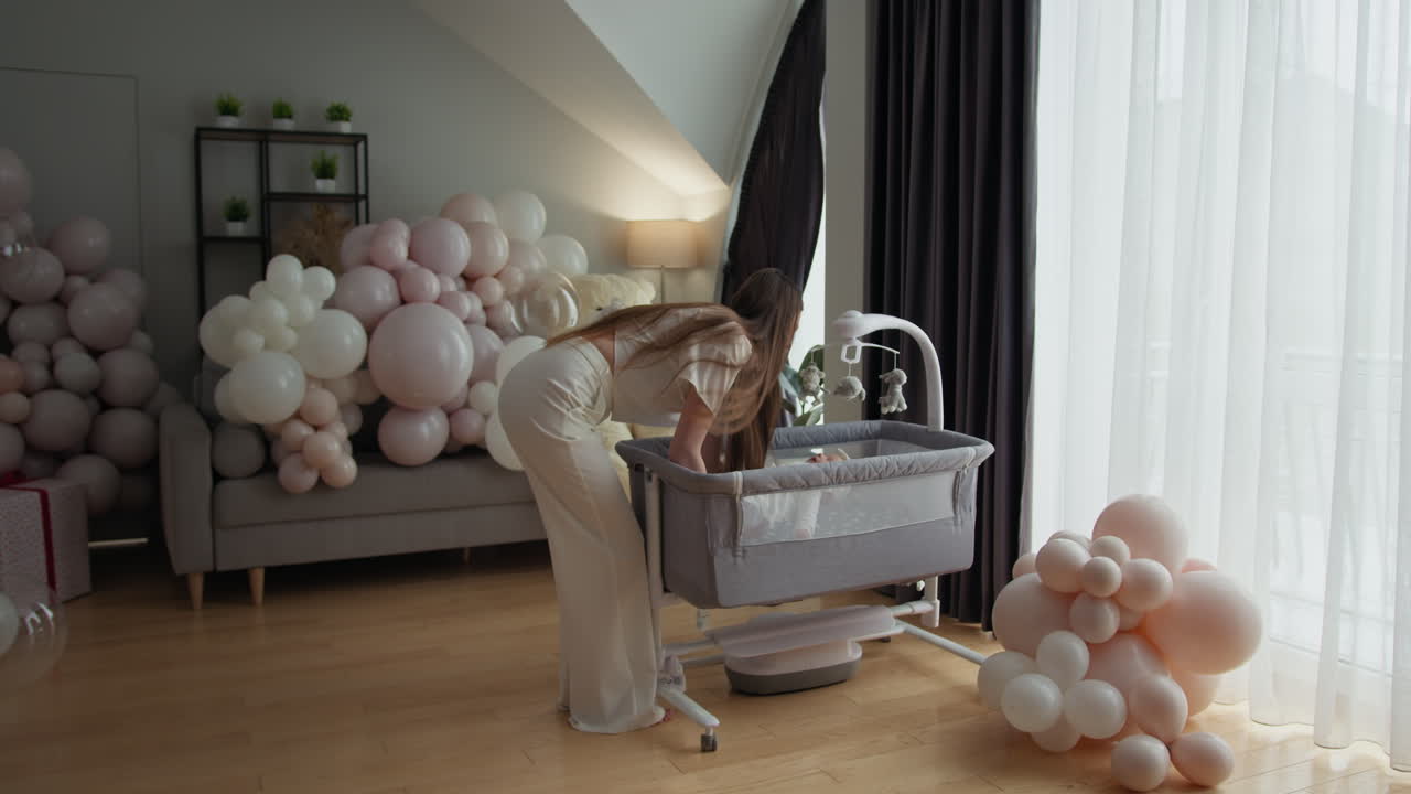 Madre che tiene amorevolmente in braccio il neonato tra palloncini festivi e l'allestimento della cameretta, celebrando la nuova vita.