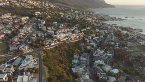 el dron vuela lentamente sobre la playa de camps bay en ciudad del cabo, sudáfrica. muchas casas en la ladera y en la lejanía una espectacular montaña de mesa.