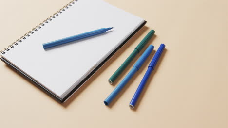 close up of blue markers with notebook on beige background, in slow motion