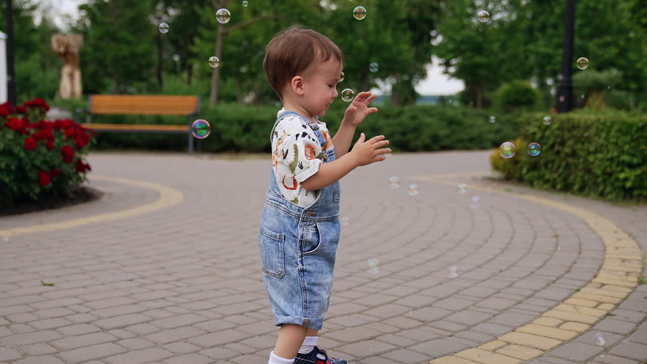 Caucasian child playing with soap bubbles in the park. Smiling baby catches the bubbles slowly.