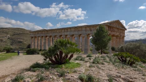 doric temple of segesta behind the trees at sunny spring day in sicily, italy with unrecognizable tourists