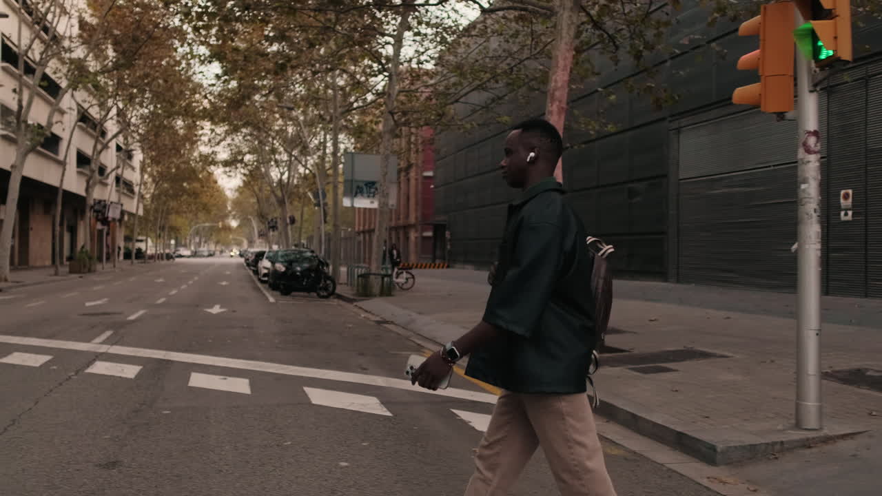 Giovane uomo con zaino e auricolari che attraversa una strada urbana