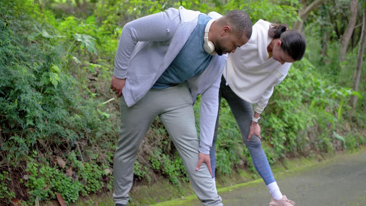 Diverse friends adjusting sweatpants, tying sneakers on forest trail starting hamstring stretches