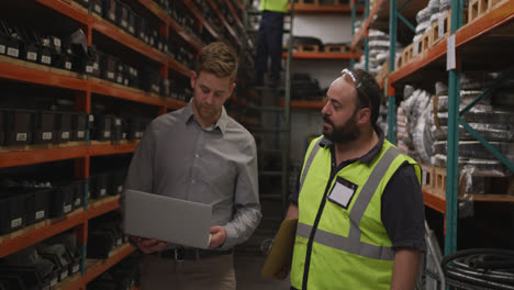 Two-Caucasian-male-factory-workers-at-a-factory-making-hydraulic-equipment-in-discussion