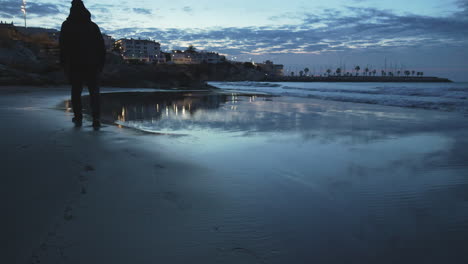 man footprints wet sand at winter beach blue hour, twilight with coastal city