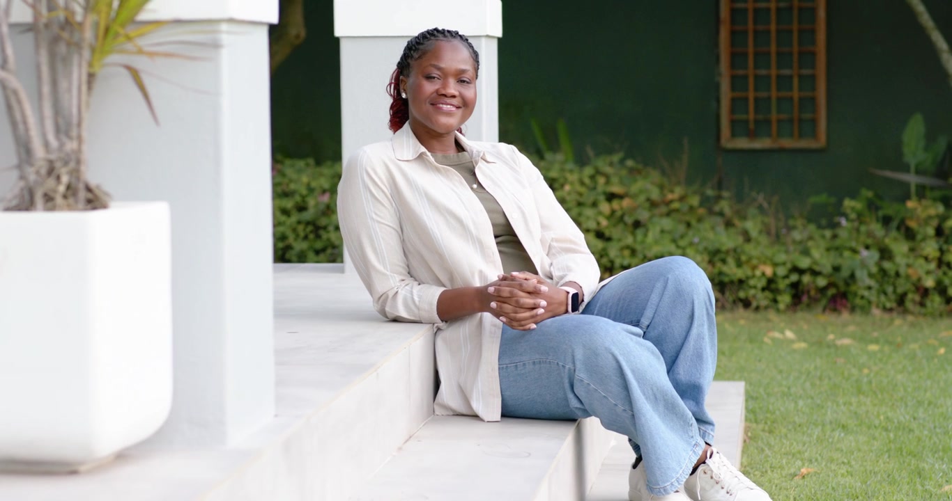 Donna afroamericana seduta sui gradini, che nota un segnale fuori campo, si appoggia, sorride e guarda in alto.