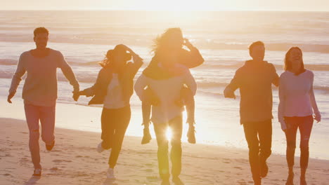 group of friends having fun running along winter beach together