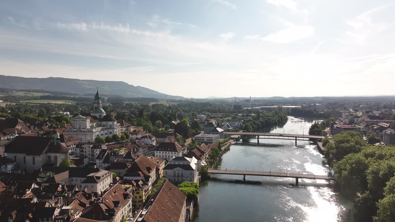 A bright aerial view showcases the city of Olten in Switzerland's Kanton Solothurn, bisected by the Aare River. The image features multiple bridges connecting the historic cityscape