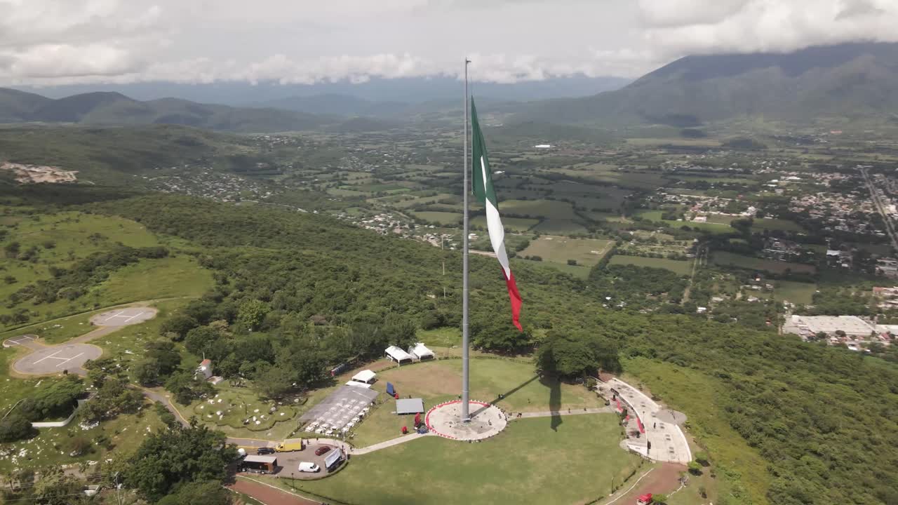 dron aéreo giratorio de gran majestuosa bandera patriótica mexicana roja, blanca y verde ondeando en el viento a lo largo del terreno montañoso durante el día
