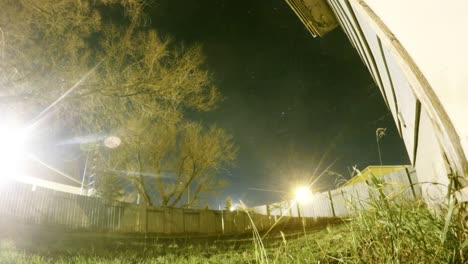 lapso nocturno - luna cayendo y estrellas volando sobre un árbol en un patio al lado de una casa