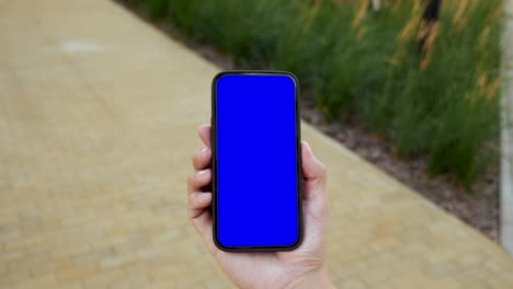 person walking and use smartphone green screen chroma key top point of view. caucasian man hold in hand phone mock-up and watching video show, surfing browsing internet. go in urban cellphone close-up