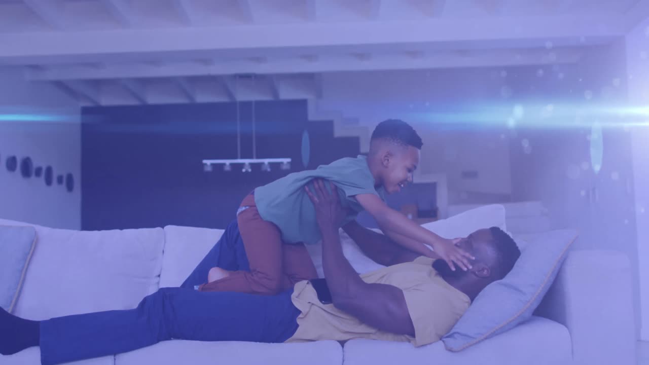 Animation of lights over happy african american father and son having fun on sofa