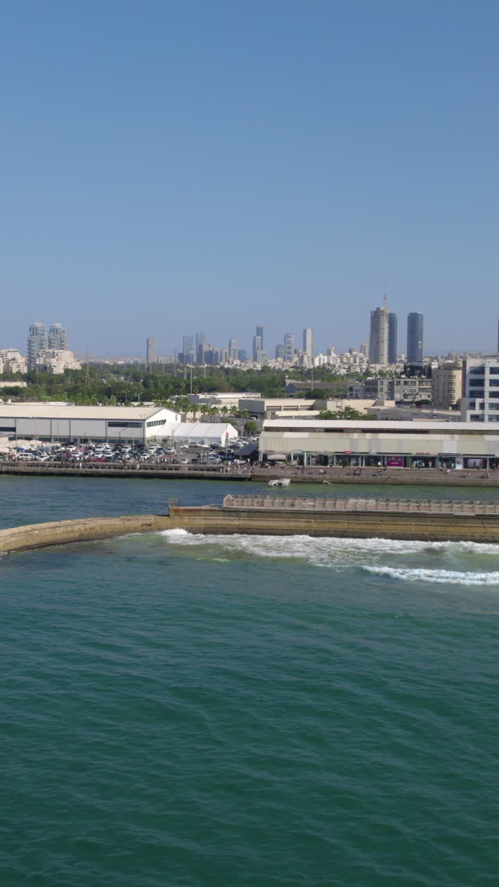 The old Tel Aviv port and the port promenade on a summer day with many residents, with the city's parks and the skyline in the background - parallax shot - vertical video