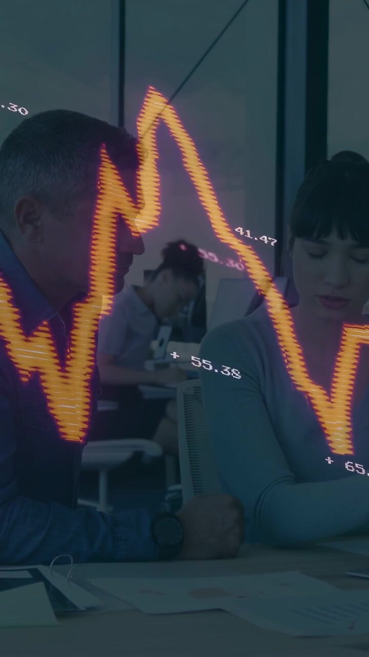 Vertical video: Waveform sweeping from left updating finance data over lead man, woman reading docs