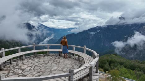 aerial orbit of woman looking out across scenic mountain vista viewpoint in theth, albania, admiring rugged peaks and deep valleys