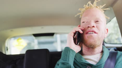 happy albino african american man with dreadlocks sitting in car talking on smartphone