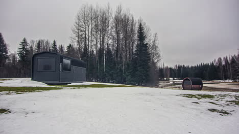 Pequeño-Edificio-De-Cabina-De-Sauna-De-Madera-En-Un-Paisaje-De-Campo-Nevado,-Lapso-De-Tiempo-De-Fusión