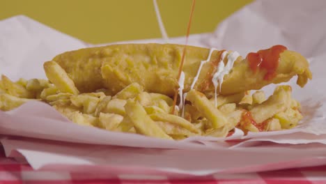 studio shot of traditional british takeaway meal of fish and chips covered with sauces