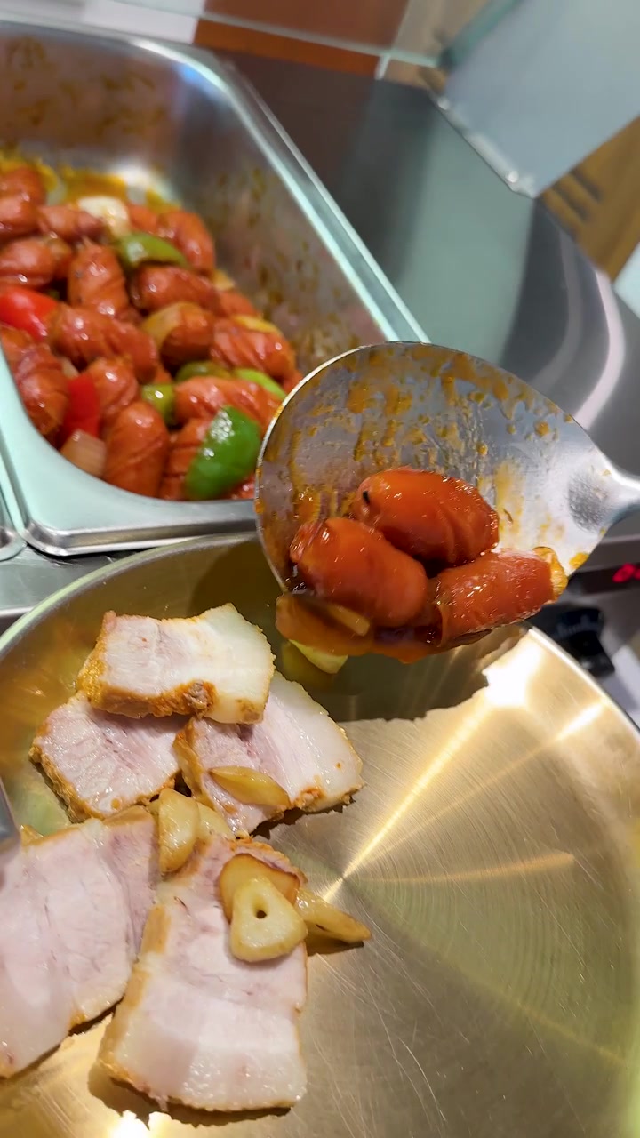 Metalske øser krydrede pølser fra en buffetbakke over på en tallerken med flæskesteg