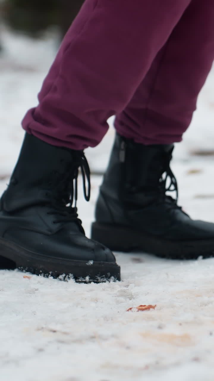 vista lateral de una persona con botas negras saltando en una pierna en un entorno al aire libre cubierto de nieve, el calzado crea pequeñas hendiduras en la nieve