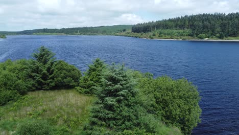 Idyllic-blue-water-reservoir-lake-woodland-hiking-walk-aerial-reveal-view-rising-above-trees