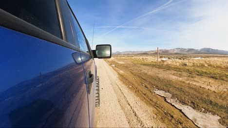 driving along the pony express trail in utah's west desert towards the snowy mountains - view from the side of a blue truck