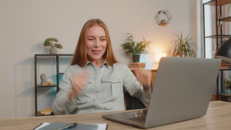 excited caucasian woman working on laptop shocked by sudden victory sitting at home office desk