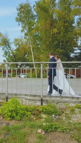 lovely newly wedded couple walks along metal fence in green park on sunny autumn day travel shooting