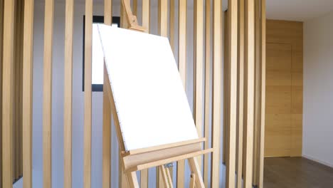 Slow rotating shot of a blank canvas standing on a wooden easel in a studio