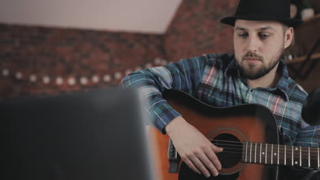 young male musician recording and streaming a video tutorial, playing guitar at home