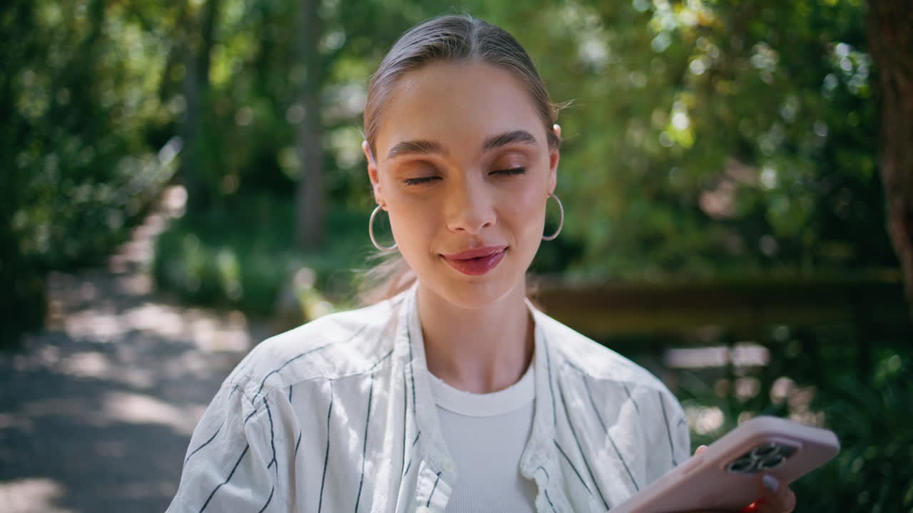 멋진 소녀가 드폰으로 문자 메시지를 보내며 녹색 자연을 가까이에서 볼 수 있습니다. 여자가 스크롤합니다.