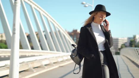 young woman talking on mobile phone on bridge in sunlight