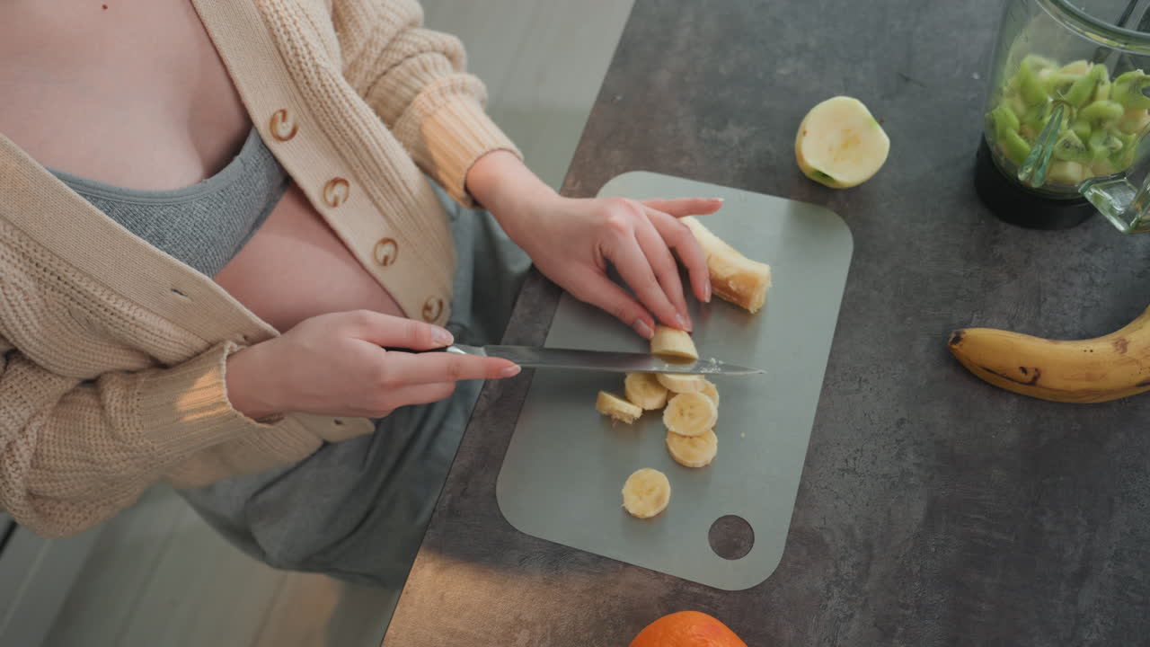 La mamma prepara uno spuntino sano. Una donna incinta prepara uno spuntino nutriente. La futura mamma sistema la frutta per il pasto. La futura mamma taglia a fette le banane per una colazione veloce e sana