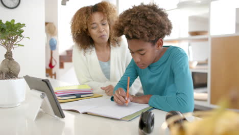 Happy-african-american-mother-helping-her-son-with-homework-using-tablet-in-kitchen,-slow-motion