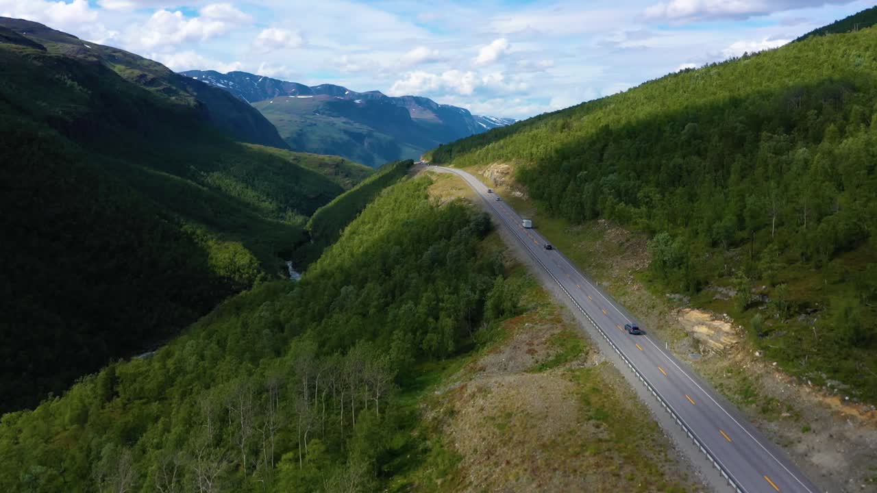 Drone shot of cars and a motorhome, driving on a highland, canyon road, Polar alpines in the background, sunny day, in Norway - rising, drone shot