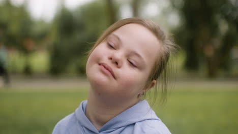 close-up view of a little girl with down syndrome looking at camera sitting on the grass in the park