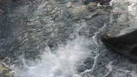 fast-moving clear water rushes over dark river rocks in natural daylight, captured with a steady overhead camera angle