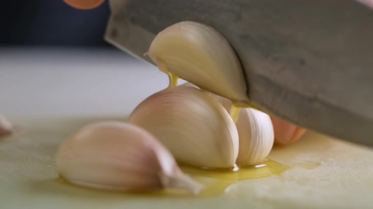 Chef che affetta spicchi d'aglio freschi su un tagliere