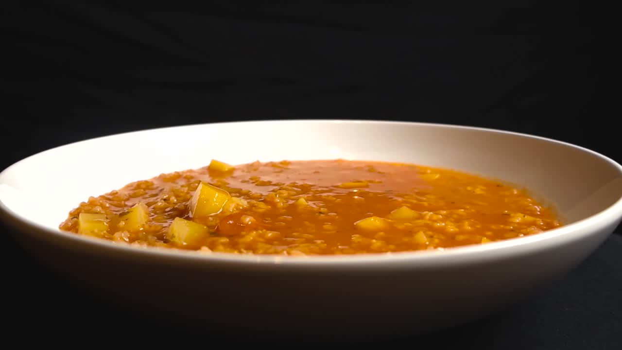 Студийный крупный план шелковистого томатного супа с рисом и кусочками картофеля в белой миске на темном фоне