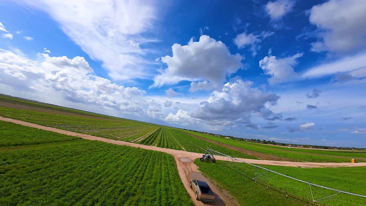 Tesla Cybertruck riding along the irrigational system in the farm field. Following the fast electric car from FPV drone.