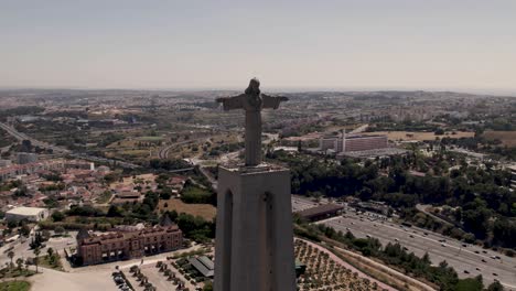 front facing of majestic statue of christ the king against almada cityscape, aerial panning shot