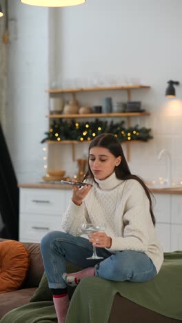 mujer hablando por teléfono y bebiendo cócteles en el acogedor salón decorado de navidad