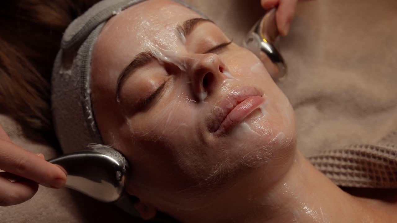 Mulher recebendo massagem facial com globos de crioterapia em spa.